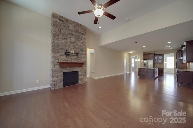 unfurnished living room with a stone fireplace, baseboards, and dark wood-style flooring