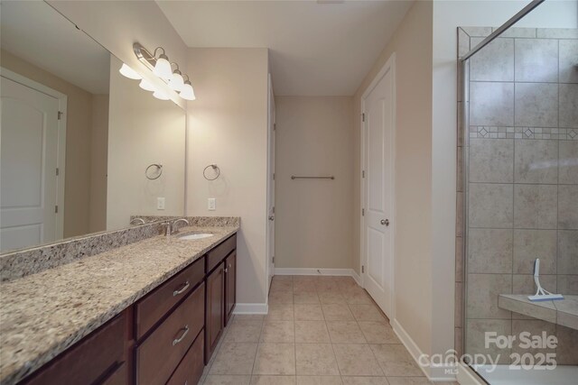 bathroom with vanity, tile patterned flooring, baseboards, and a tile shower