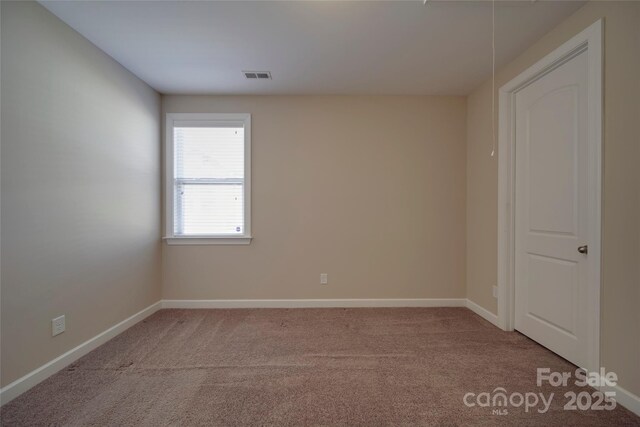 carpeted spare room featuring visible vents, attic access, and baseboards