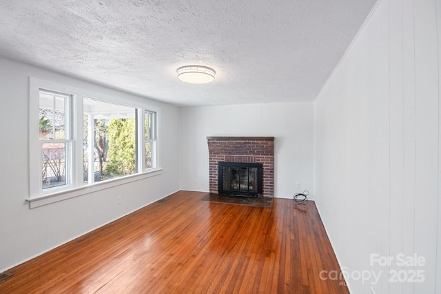 unfurnished living room featuring visible vents, a textured ceiling, a brick fireplace, and hardwood / wood-style flooring