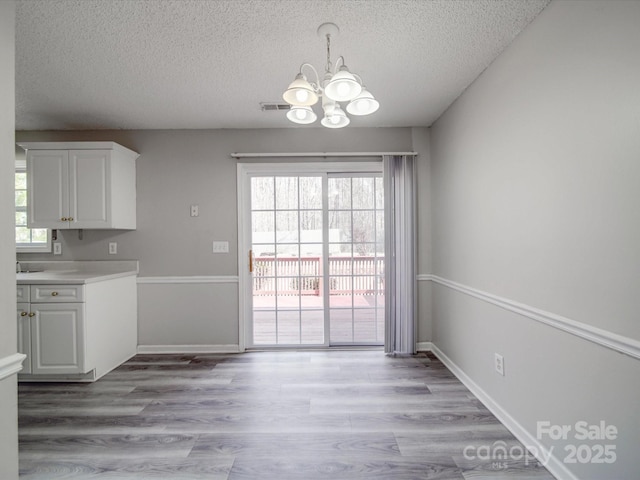 unfurnished dining area featuring visible vents, light wood-style flooring, a textured ceiling, an inviting chandelier, and baseboards