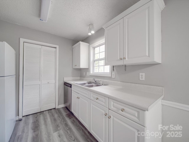 kitchen with a sink, stainless steel dishwasher, wood finished floors, freestanding refrigerator, and white cabinets