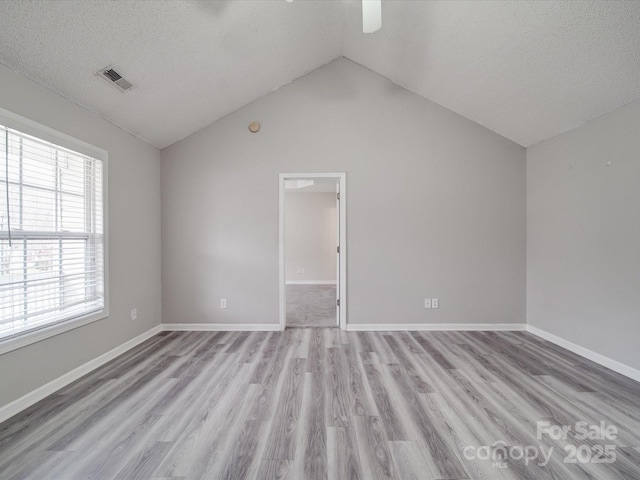 empty room featuring light wood-type flooring, visible vents, a textured ceiling, baseboards, and vaulted ceiling