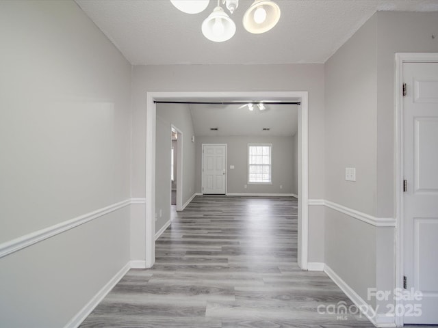 corridor with a textured ceiling, wood finished floors, baseboards, a chandelier, and vaulted ceiling