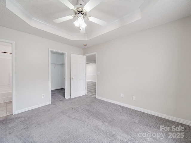 unfurnished bedroom featuring a walk in closet, a raised ceiling, carpet, and a textured ceiling