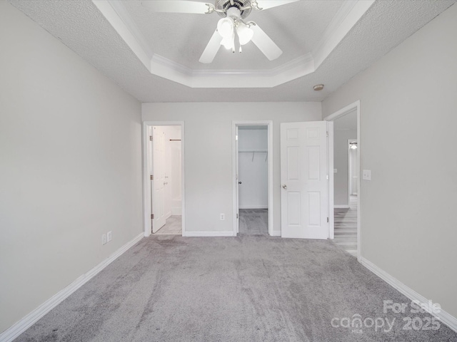 unfurnished bedroom with carpet flooring, baseboards, a walk in closet, and a tray ceiling