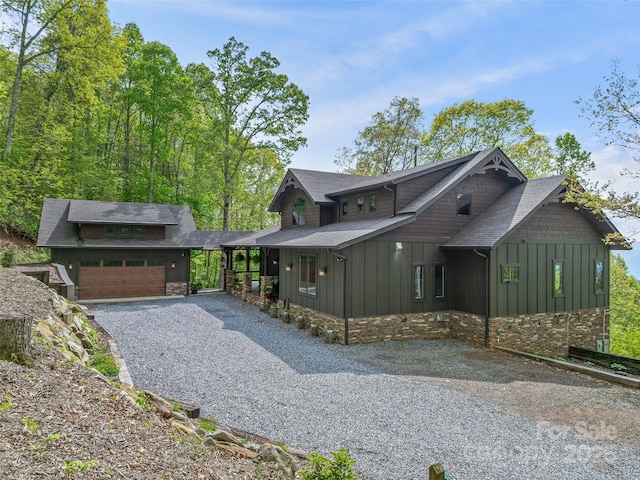 chalet / cabin featuring gravel driveway, a shingled roof, a garage, stone siding, and board and batten siding