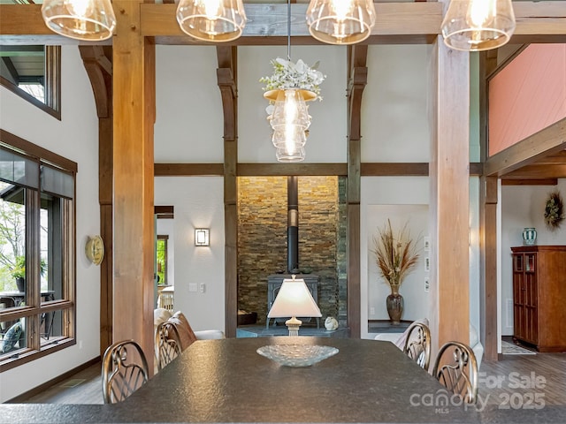 dining space featuring a towering ceiling, a notable chandelier, wood finished floors, and a wood stove