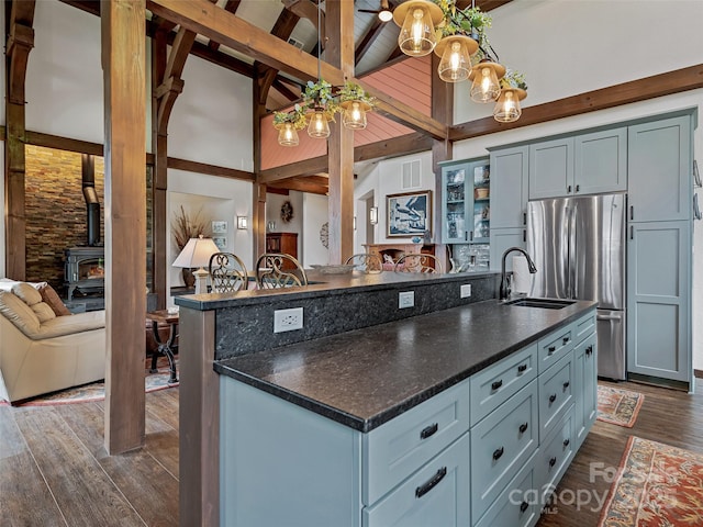 kitchen featuring dark wood finished floors, beamed ceiling, freestanding refrigerator, a wood stove, and a sink