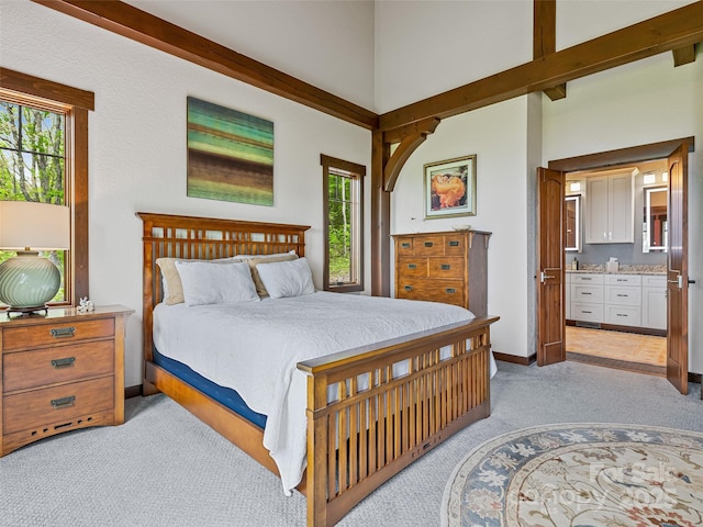 bedroom featuring baseboards, light colored carpet, beam ceiling, a high ceiling, and ensuite bath