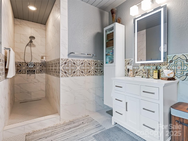 full bathroom featuring tile walls, walk in shower, vanity, and a textured wall