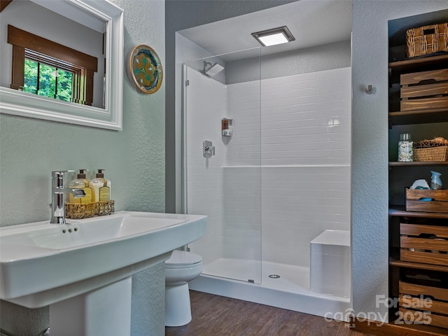 bathroom with a shower stall, toilet, a textured wall, and wood finished floors