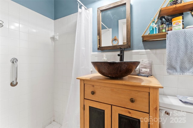 bathroom with a tile shower, toilet, tile walls, and vanity