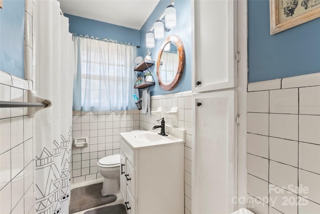 bathroom featuring wainscoting, toilet, tile walls, and vanity