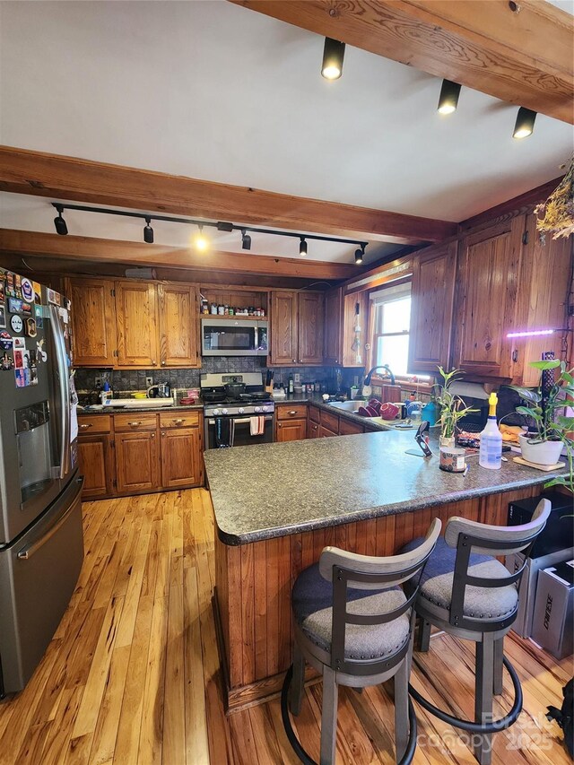 kitchen featuring decorative backsplash, light wood-style flooring, appliances with stainless steel finishes, brown cabinets, and a peninsula