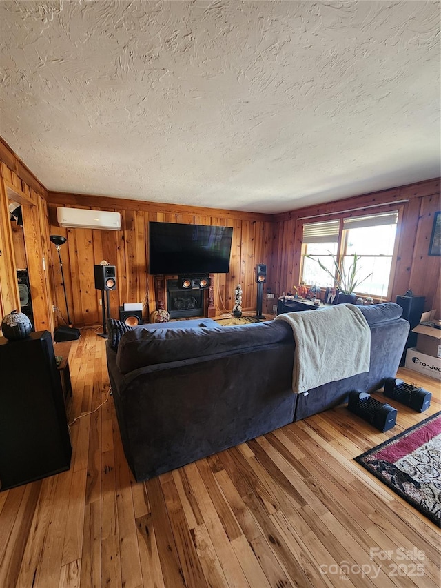 living room with a textured ceiling, wooden walls, light wood-type flooring, and a wall mounted AC