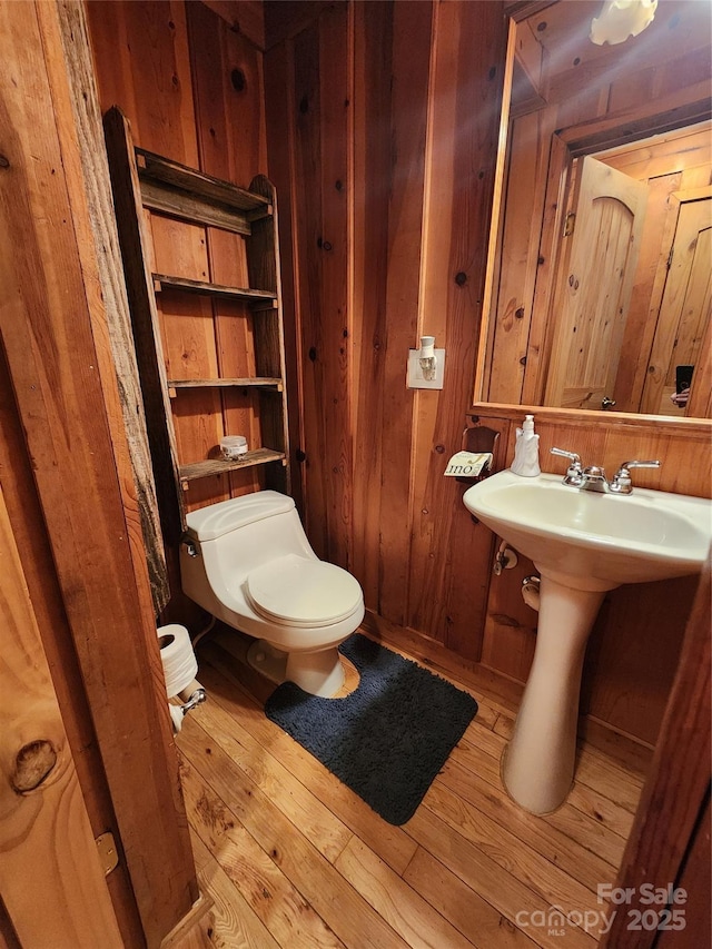 half bathroom with a sink, toilet, wooden walls, and hardwood / wood-style flooring