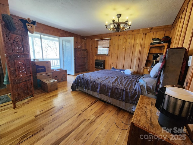 bedroom featuring heating unit, light wood-style floors, an inviting chandelier, and wood walls