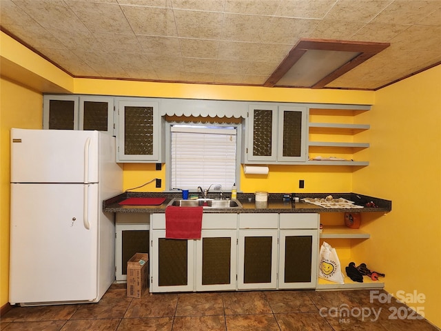 kitchen featuring open shelves, freestanding refrigerator, a sink, glass insert cabinets, and dark countertops