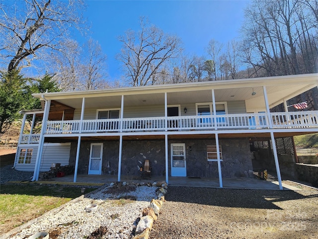 back of property with stone siding, a wooden deck, and a patio