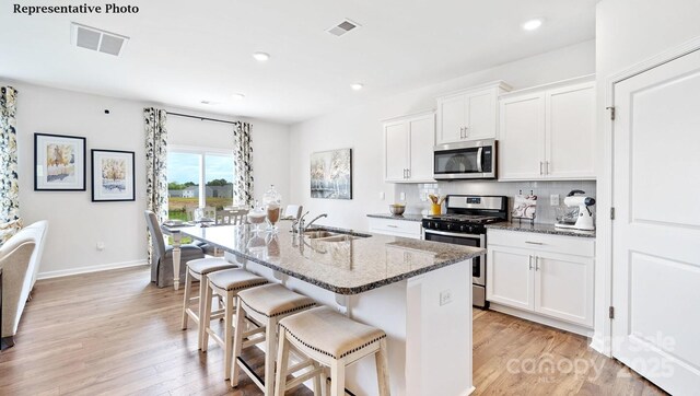 kitchen featuring visible vents, backsplash, an island with sink, stainless steel appliances, and a sink