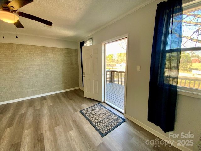 doorway to outside with brick wall, a textured ceiling, baseboards, and wood finished floors