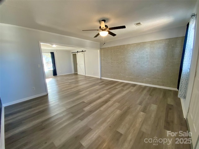 empty room with visible vents, wood finished floors, a barn door, brick wall, and ceiling fan