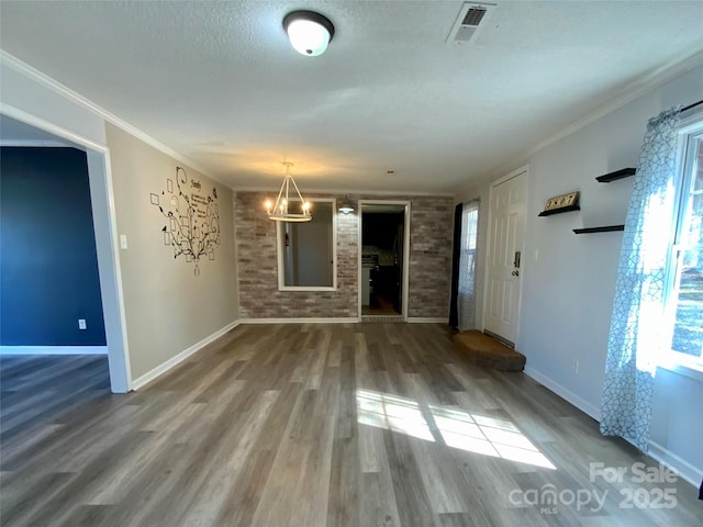 unfurnished living room featuring visible vents, wood finished floors, brick wall, and ornamental molding