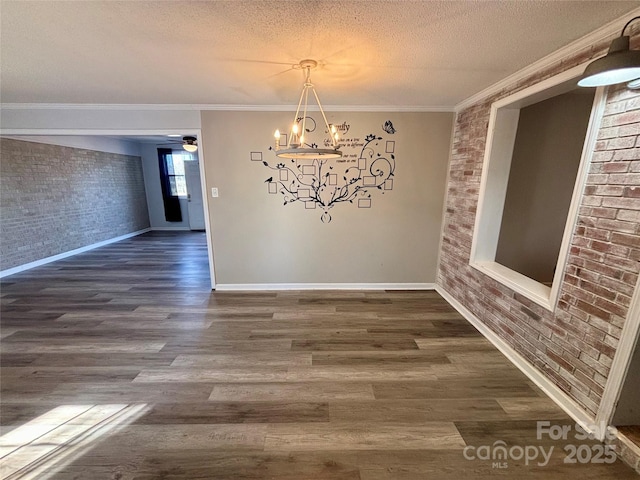 unfurnished dining area featuring ornamental molding, a textured ceiling, wood finished floors, brick wall, and baseboards