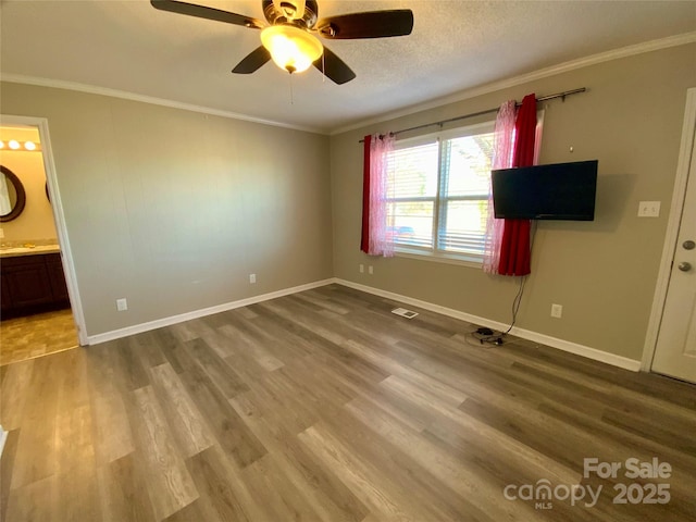 unfurnished bedroom with ornamental molding, ensuite bathroom, a textured ceiling, wood finished floors, and baseboards