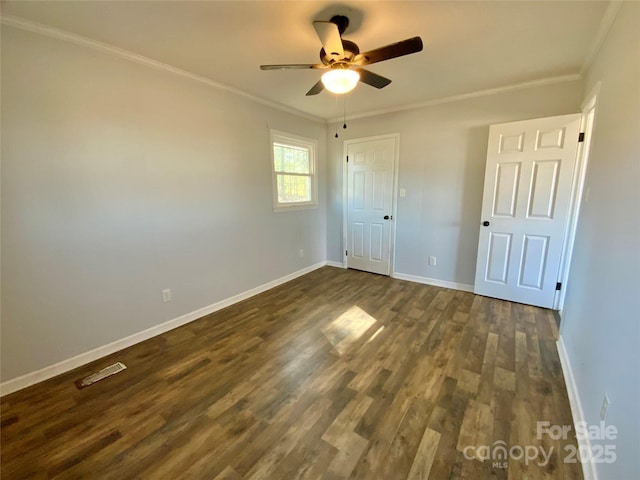 unfurnished bedroom with dark wood finished floors, visible vents, crown molding, and baseboards