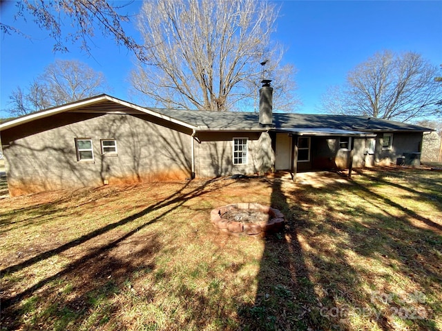 back of property with a chimney, a lawn, and an outdoor fire pit