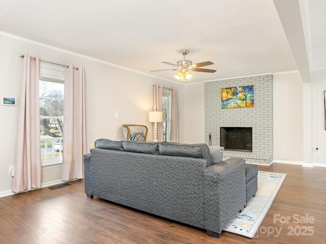 living area featuring ceiling fan, baseboards, ornamental molding, a fireplace, and wood finished floors