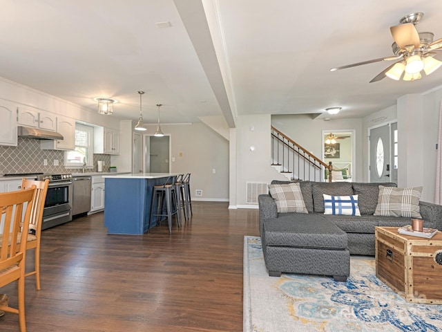 living area featuring stairway, baseboards, a ceiling fan, and dark wood-style flooring