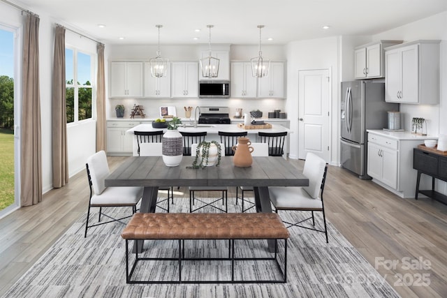 kitchen with light wood-style flooring, a kitchen island with sink, stainless steel appliances, white cabinets, and light countertops