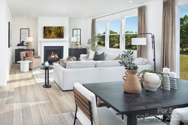 living room featuring recessed lighting, plenty of natural light, a warm lit fireplace, and light wood finished floors