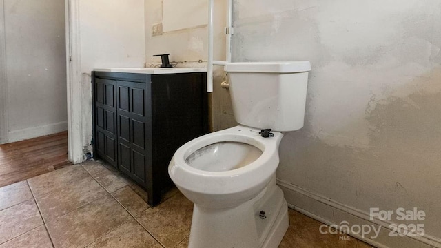 half bathroom with baseboards, toilet, vanity, and tile patterned flooring