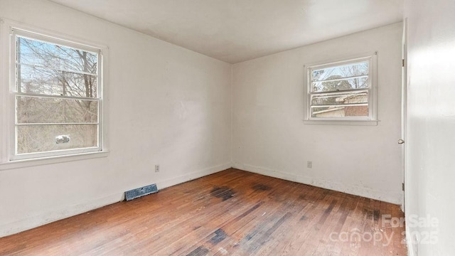 unfurnished room featuring hardwood / wood-style flooring, baseboards, and visible vents