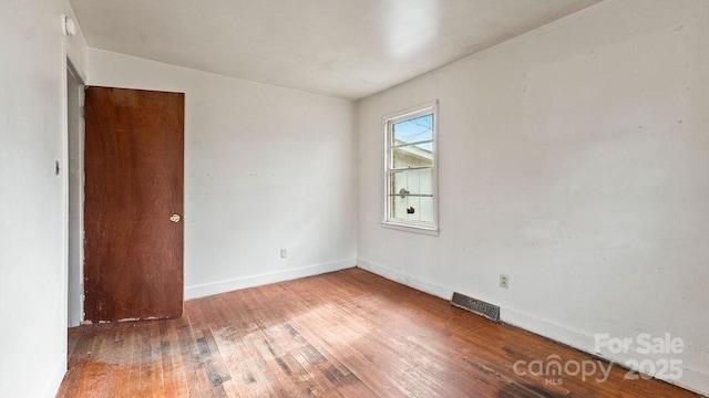 unfurnished room with hardwood / wood-style floors, baseboards, and visible vents