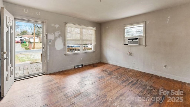 empty room featuring hardwood / wood-style flooring, cooling unit, baseboards, and visible vents