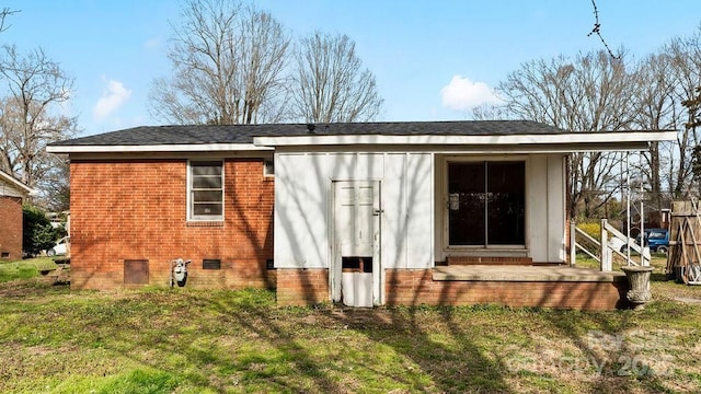 rear view of property with crawl space, brick siding, and a yard