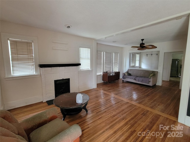 living room with a fireplace, plenty of natural light, wood finished floors, and a ceiling fan