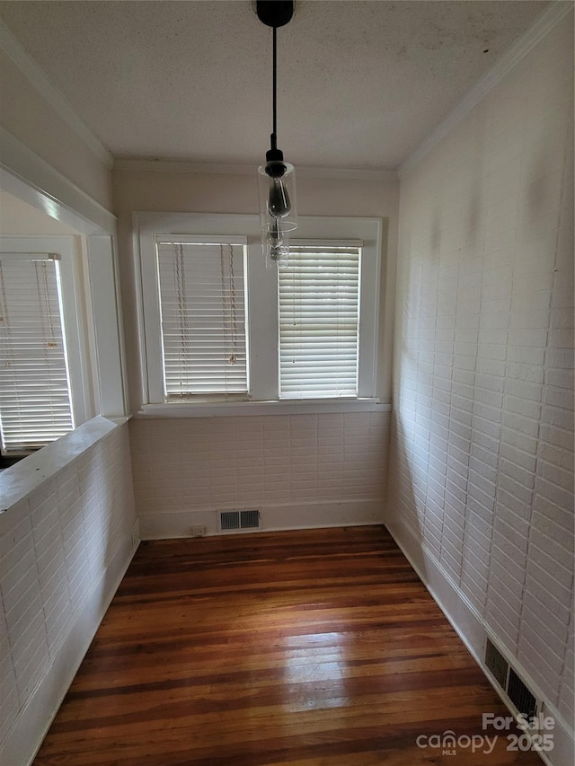 unfurnished dining area with a textured ceiling, dark wood-type flooring, visible vents, and ornamental molding