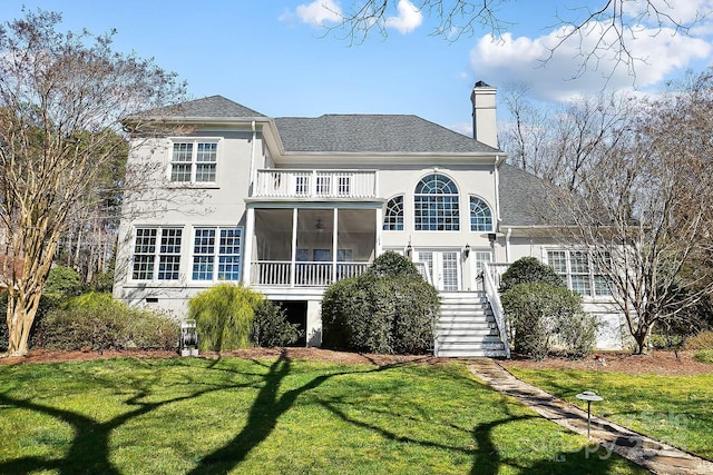 rear view of property featuring a balcony, stairway, a yard, a sunroom, and a chimney