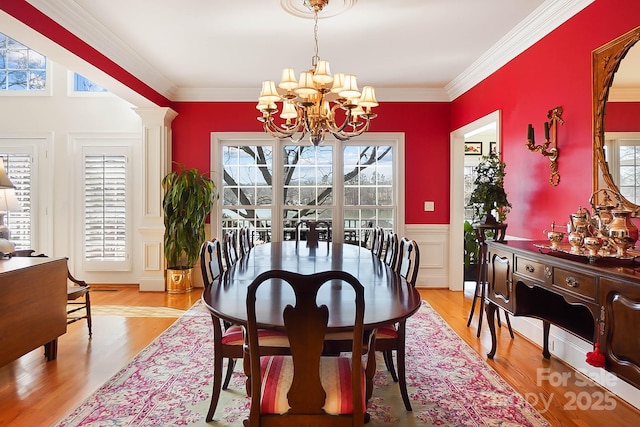 dining room featuring light wood-type flooring, a notable chandelier, ornamental molding, and wainscoting