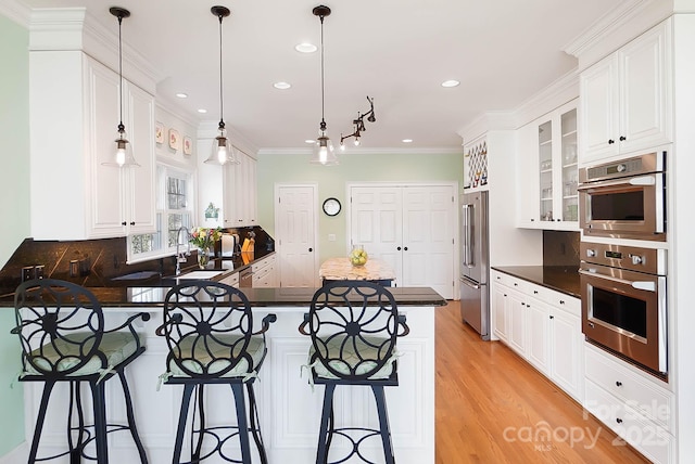 kitchen featuring a peninsula, a sink, appliances with stainless steel finishes, white cabinetry, and dark countertops