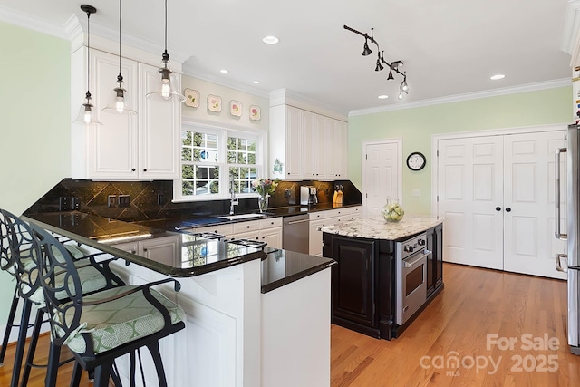 kitchen featuring light wood finished floors, a sink, stainless steel appliances, white cabinetry, and a kitchen breakfast bar