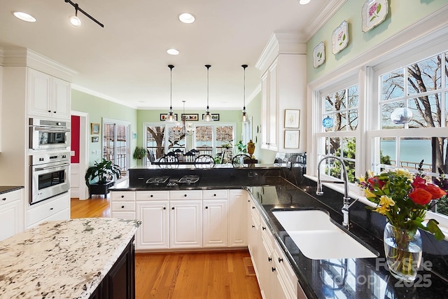 kitchen with a peninsula, crown molding, light wood-style floors, and a sink