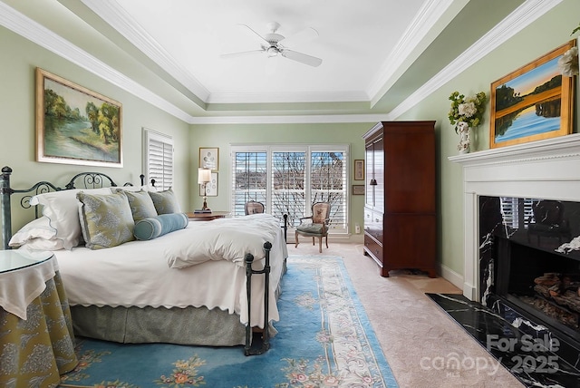 bedroom featuring a high end fireplace, crown molding, a tray ceiling, and carpet