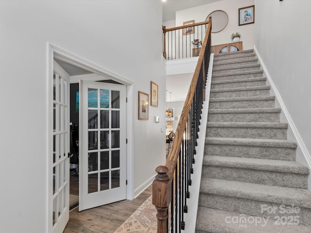 staircase with wood finished floors, french doors, baseboards, and a towering ceiling